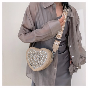 Détail d'un sac bandoulière beige en forme de cœur avec strass et bandoulière tissée