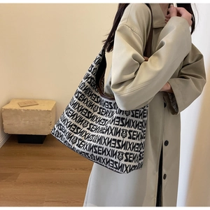 Close-up of beige knitted hobo bag featuring letter prints and brown leather trim detailing