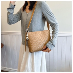 Close-up of woven PU leather shoulder bag in caramel brown with elegant pearl pendant