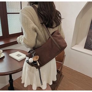 Detail of a brown suede rectangular shoulder bag with creative baseball glove charm