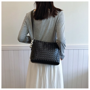 Detail of black woven PU shoulder bag with silver sphere charm worn on shoulder