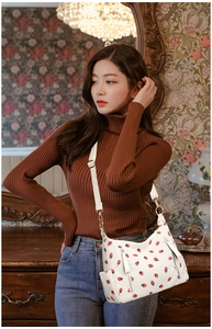 Detail showing the strawberry pattern and metal buckle on the cream white crossbody bag