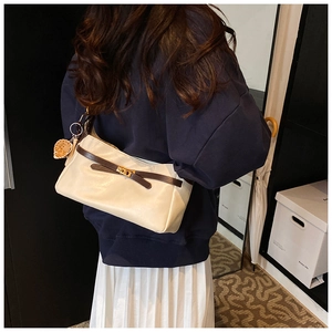 Detail of a minimalist two-tone PU leather shoulder bag with a gold lock and bear charm