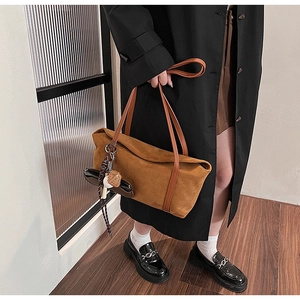 Close-up of brown suede tote bag with leather straps and a cute plush keychain charm