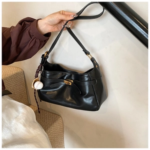 Detail of black PU leather shoulder bag with gold buckle and baseball charm accessory