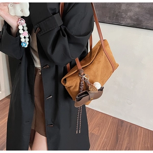 Brown suede shoulder bag detail with leather strap and decorative baseball charms