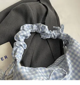 Detail of light blue plaid fabric bag featuring pleated shoulder strap and metal zipper