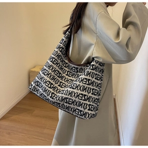 Detail shot of a large knit tote bag with black and white monogram and brown leather trim