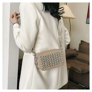Fashionable beige PU leather crossbody bag with silver sphere studs on a female model