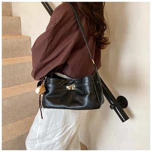 Detail view of black matte leather shoulder bag with golden clasp and white spherical charm