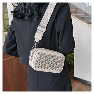 Detail view of beige camera bag with silver rivets and wide woven crossbody strap on model