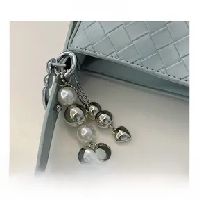 Close-up of light blue woven leather bag with silver heart and pearl hardware charms