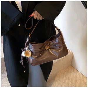 Detail of dark brown PU leather shoulder bag with gold clasp and woven pendant decoration