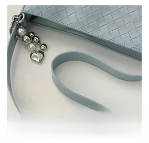 Close-up of woven light blue PU leather handbag with pearl and heart-shaped charms