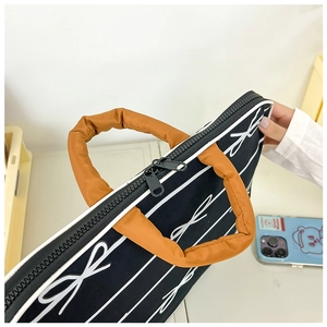 Detail of laptop bag showing orange padded handle and black bow pattern fabric