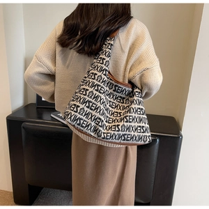 Detail view of knitted tote bag with black letter patterns and brown leather strap on model