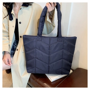 Detail showing deep blue quilted nylon tote bag with V-shaped stitching on model