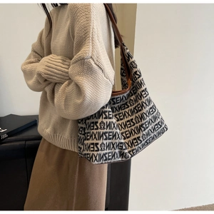 Detail of knitted tote bag with SENXIN letter print and leather handle on a model