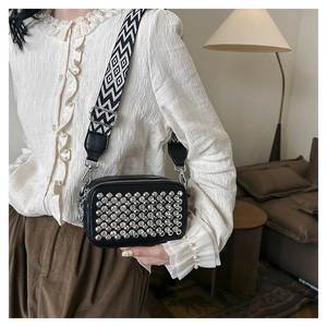 Detail of black crossbody camera bag with silver rivets and wide geometric patterned strap