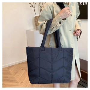 Detail of navy blue quilted nylon tote bag worn over the shoulder with beige coat