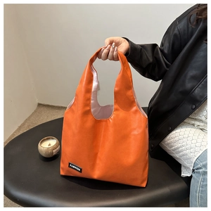 Detail of a vibrant orange PU leather handbag featuring a black Fashion logo tag
