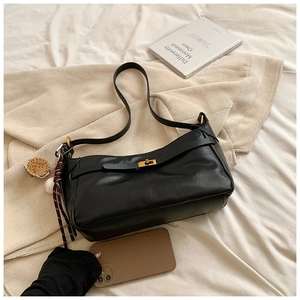 Minimalist black PU leather shoulder bag with gold clasp and sports charm on striped bedding