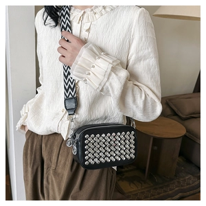 Detail of a black PU leather crossbody bag featuring silver rivets and a wavy wide strap