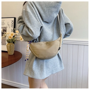 Detail of khaki crescent crossbody bag with braided rope charm and fashion label