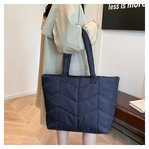 Detail of navy blue quilted nylon tote bag with V-pattern stitching on female shoulder