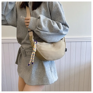 Detail view of beige crescent bag featuring a colorful woven rope charm and fashion tag