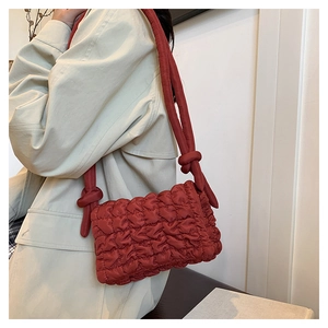 Detail der dunkelroten gesteppten Nylon-Schultertasche mit Knotengurt auf beigem Mantel