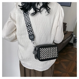 Detail of black leather crossbody bag featuring silver rivets and a jacquard shoulder strap