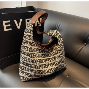 Chic knitted shoulder bag with logo pattern and brown leather trim on a black sofa
