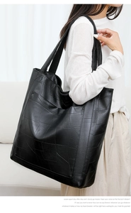 Detail of a large black PU leather tote bag with geometric patchwork on a female model
