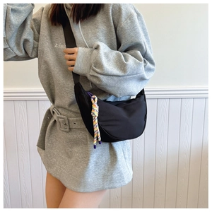 Minimalist black crescent canvas shoulder bag with colorful woven rope charm on model