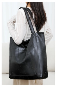 Detailed view of black PU leather tote bag featuring geometric patchwork on shoulder