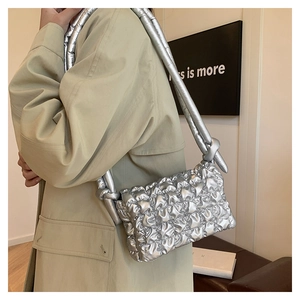 Detail der silbernen Falten-Puffertasche mit Knotengurt an einem Modell im Trenchcoat