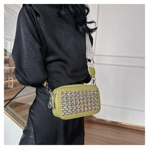 Close-up of green PU crossbody bag with silver studs and wide woven shoulder strap