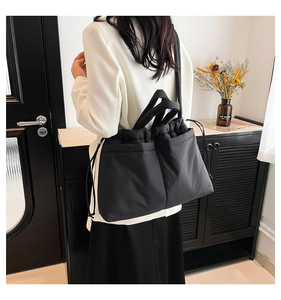 Detail of black quilted shoulder bag featuring drawstring closure and large front pockets