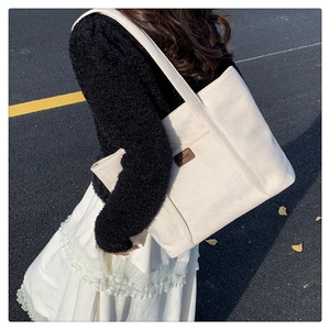 Detail of off-white canvas tote bag featuring wide strap and brown leather logo patch