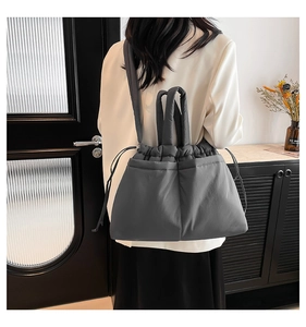 Detail of grey quilted shoulder bag with drawstring closure on model in a modern interior