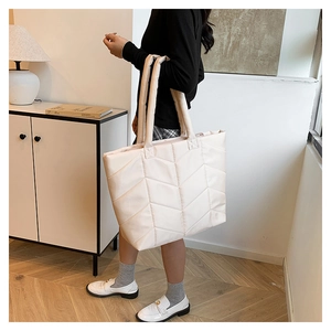 Detail view of a beige quilted nylon tote bag featuring wide V-shaped stitching and soft handles