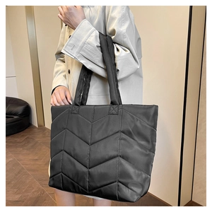 Detailed side view of black quilted nylon tote bag worn by model in minimalist interior
