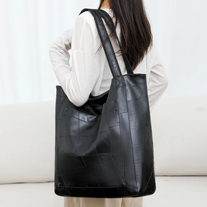 Detail view of large black geometric PU leather tote bag worn by a model in soft indoor light