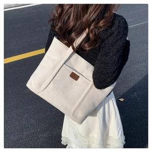 Outdoor shot of a beige suede tote bag with brown logo patch and long shoulder straps