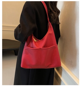 Detail view of a large red PU leather tote bag with functional front pockets worn by model