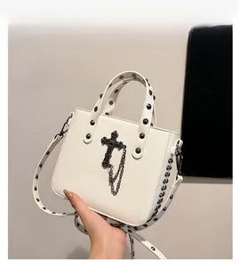 Detail view of a white PU leather handbag with black rivets and a cross pendant accessory