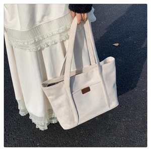 Detailed close-up of cream corduroy tote bag featuring a leather logo patch and soft texture