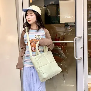 Dettaglio di una borsa a tracolla trapuntata verde chiaro con spessi manici in tessuto su modella