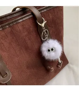 Detail of creative white fluffy monster keychain with big eyes on brown suede tote bag